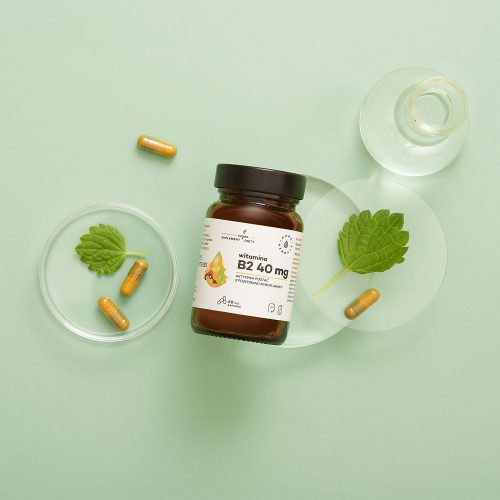 Butelka Witamina B2 R-5-P 40 mg ryboflawina kapsułki 60 szt_2 spoczywa na jasnozielonej powierzchni, otoczona szklanymi płytkami Petriego, zielonymi liśćmi i luźnymi kapsułkami.