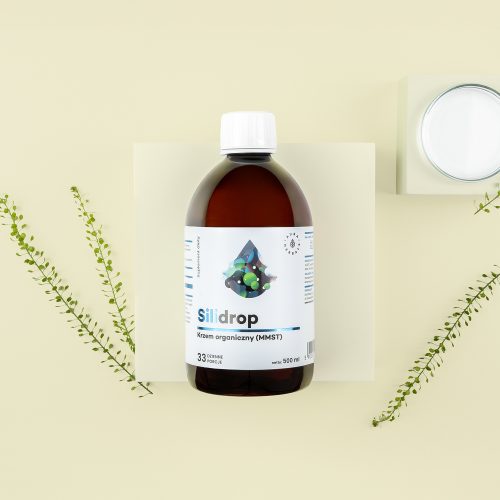 Brązowa butelka z etykietą Silidrop-krzem-organiczny-MMST-plyn-500-ml_1500x1500_2 znajduje się na jasnym tle z zielonymi gałązkami i okrągłym pojemnikiem w pobliżu.