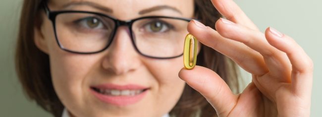 Lekarz trzyma kapsułkę z kwasami omega-3, które spożywa się w ilości 250 mg/dobę