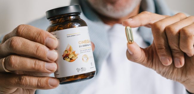 Mężczyzna trzyma w dłoni suplement diety z kwasami omega-3