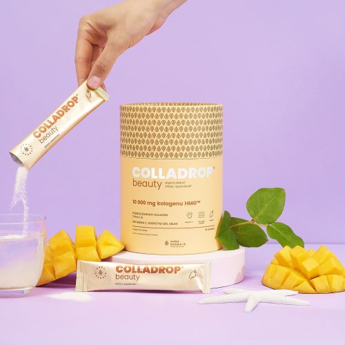 Ręka wsypuje do szklanki zawartość saszetki z proszkiem „colladrop-beauty-mango-HMG-saszetki-6_1500x1500”. Na fioletowym tle widoczne są opakowanie produktu, kawałki mango, zielona gałązka oraz biała rozgwiazda.