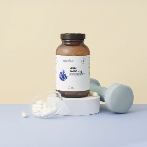 Butelka o nazwie „MSM-1400-mg-siarka-organiczna-kapsułki-120-szt_2_1500x1500” stoi na białej platformie obok niebieskiego hantla, a w pobliżu leżą rozrzucone białe kapsułki.